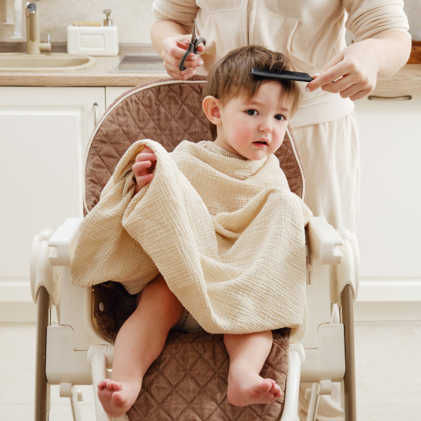母亲在厨房里剪着蹒跚学步的男孩。自己的理发师剪小孩的头发。一岁六个月的孩子图片下载