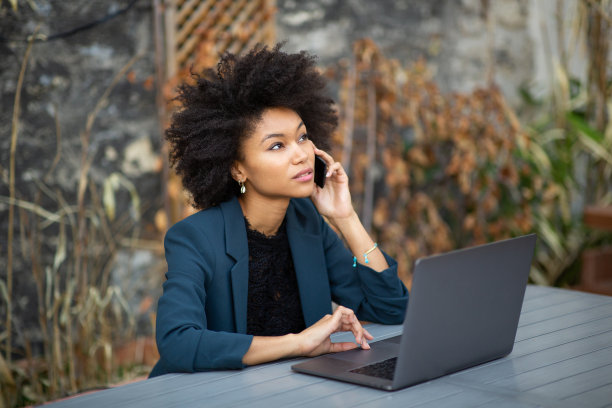 年轻的黑人女性专业人士在用手机聊天，笔记本电脑放在咖啡桌上图片下载