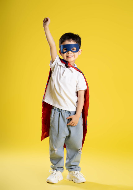 一个穿着超级英雄衬衫的男孩在黄色背景上摆姿势的全身照片图片下载