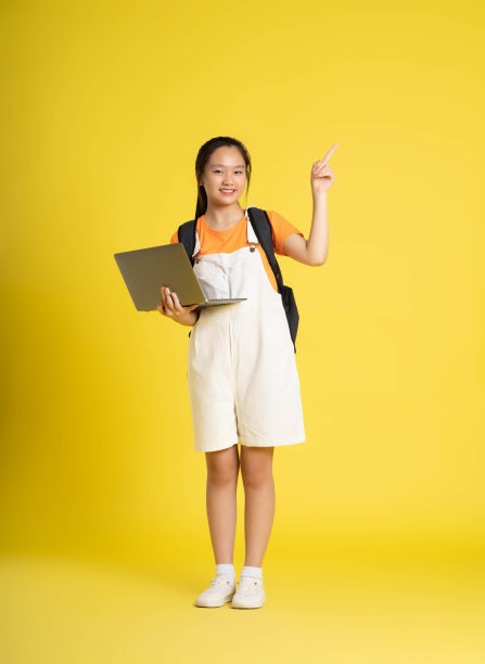漂亮的亚洲女学生用黄色背景的笔记本电脑图片下载