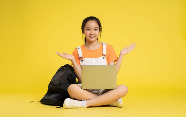 漂亮的亚洲女学生坐在黄色背景上使用笔记本电脑图片下载