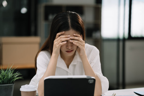 年轻悲伤的女商人捂着脸坐在桌边。桌上放着笔记本电脑、平板电脑、工作压力图片下载