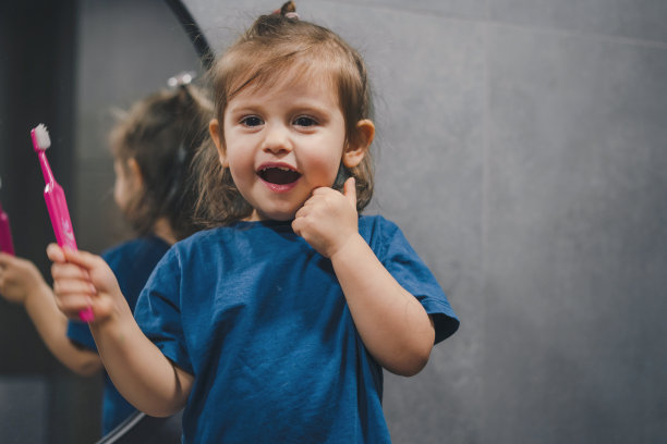 可爱漂亮的小女孩在浴室刷牙，看着镜子里的倒影。健康的牙齿。照镜子，注意晨间卫生和牙齿护理。图片下载