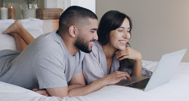 快乐，夫妻和放松与笔记本电脑在卧室观看订阅电影，下载媒体和网上购物。男人、女人和电脑技术一起在家里串流、上网或快乐图片下载