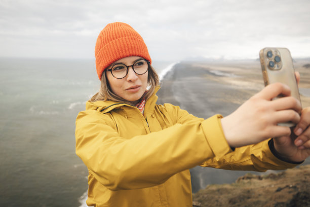 一位美女站在好望角上拍照Dyrhólaey。冰岛图片下载