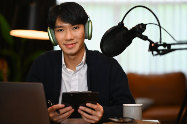 男主播戴着耳机在家庭工作室录制播客。广播，播客，博客和技术概念。图片下载