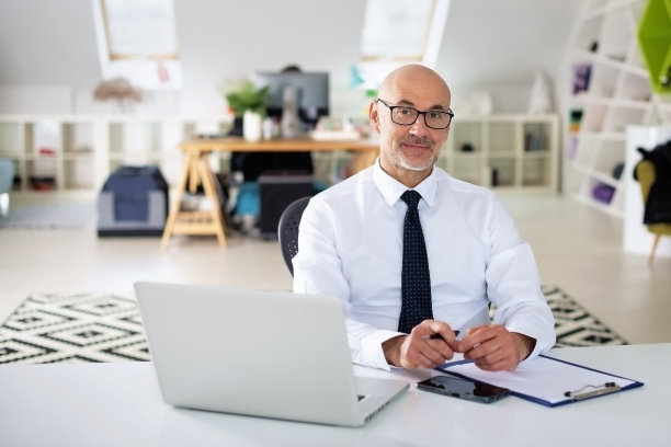 中年商人坐在办公桌旁，用笔记本电脑工作图片下载