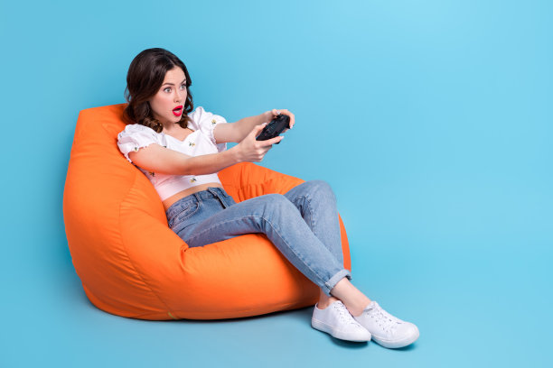 印象深刻的可爱女士的全身照片穿白色衬衫坐在豆袋看着playstation空空间孤立的蓝色背景图片下载