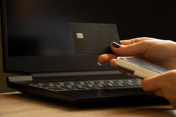 在办公室窗口附近，手持信用卡在黑色笔记本电脑旁进行在线支付的女孩图片下载