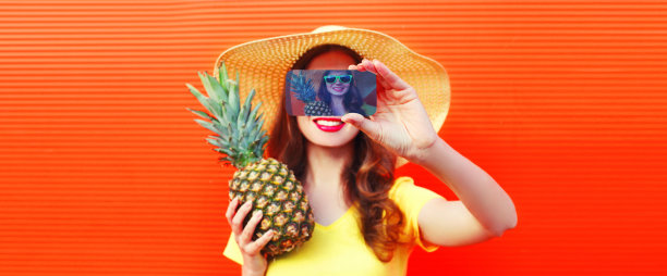 夏天肖像特写快乐微笑的女人与菠萝采取自拍智能手机戴草帽，太阳眼镜在生动的背景图片下载