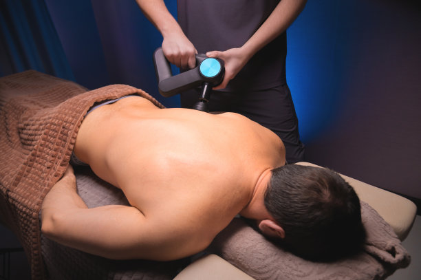 一名男客户躺下后，按摩师手持打击按摩器，对其肩部和上背部进行按摩图片下载