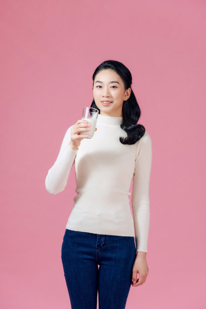 可爱健康的女人正在喝牛奶从玻璃隔离在粉红色的背景。图片下载