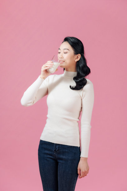 年轻女子喝杯牛奶，女性开心的微笑，孤立在粉红色背景上的自然有机概念图片下载