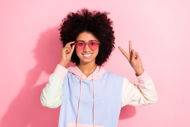 可爱的积极的女孩微笑的肖像，手臂触摸太阳镜演示v字孤立的粉红色背景图片下载