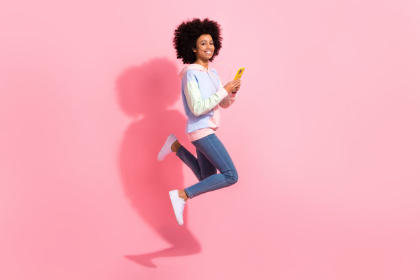 可爱时髦的小孩穿着连帽衫跳短信现代小工具孤立的粉红色背景的全长照片图片下载