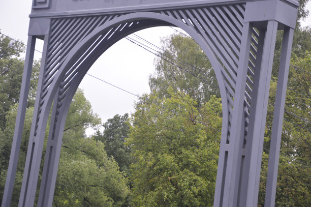 灰色的金属拱在绿树的背景下。公园的入口。装饰门。图片下载