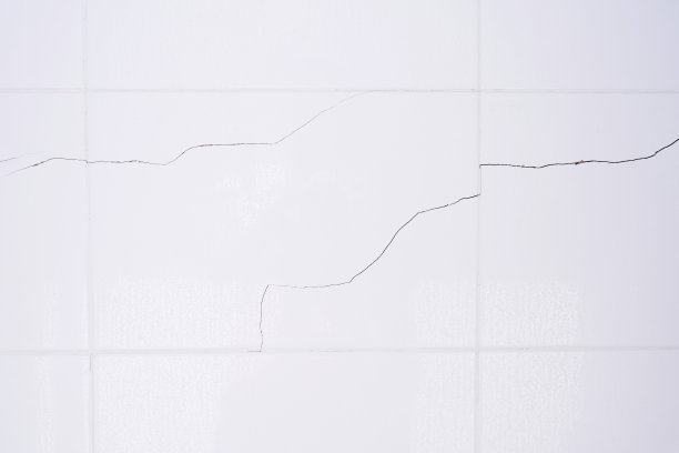 浴室里的白色瓷砖墙上有水滴。破碎、破裂的瓷砖。地震毁坏了一堵墙。图片下载