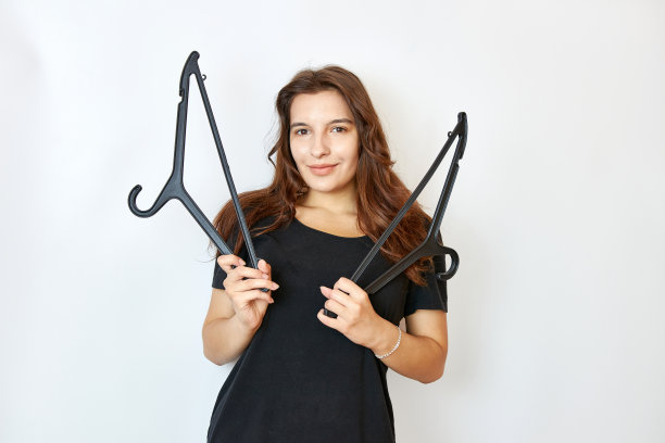 穿着黑色t恤的漂亮女孩拿着两个衣架。买衣服的概念。图片下载