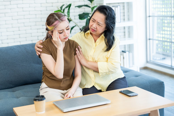 亚洲可爱的女孩头痛，用她的手触摸太阳穴，尝试或疲惫的工作与笔记本电脑旁边的支持母亲，拥抱她的肩膀。图片下载