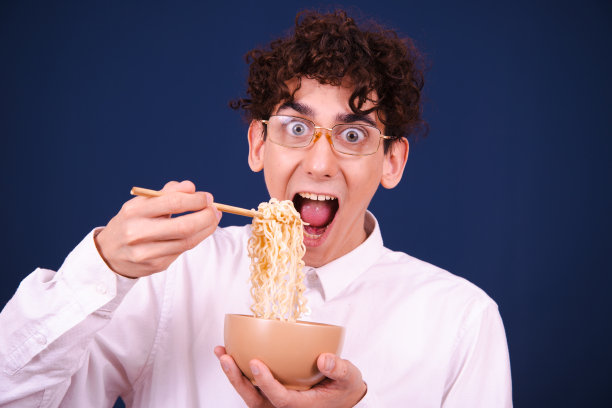有趣的情绪化的家伙吃中国面条配蔬菜。图片下载
