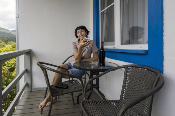 以山峦和森林为背景的阳台上的成熟女人，在森林阳台上的一张敞开的桌子上喝着酒。图片下载