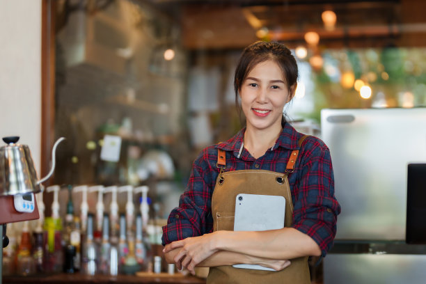 一个美丽的亚洲半身女人的肖像站在快乐的微笑与微笑的脸在那里有一个平板电脑抱在他的胸前。可在线订购饮料。女咖啡店老板图片下载