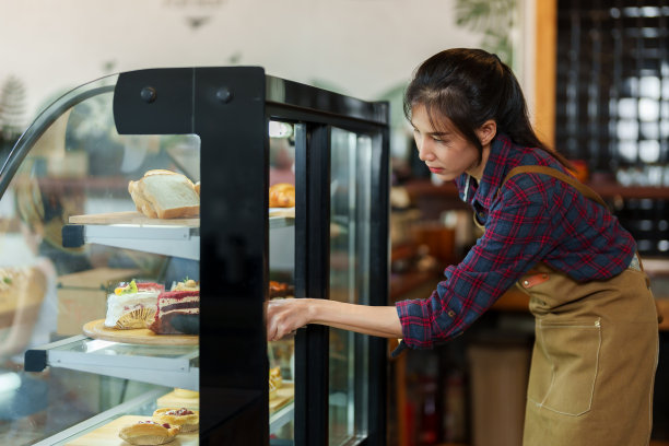 面包店老板，小型家庭企业美丽的亚洲女孩在顾客点单后在玻璃面包店拿起蛋糕，送给坐在咖啡馆里吃咖啡饮料的顾客。图片下载