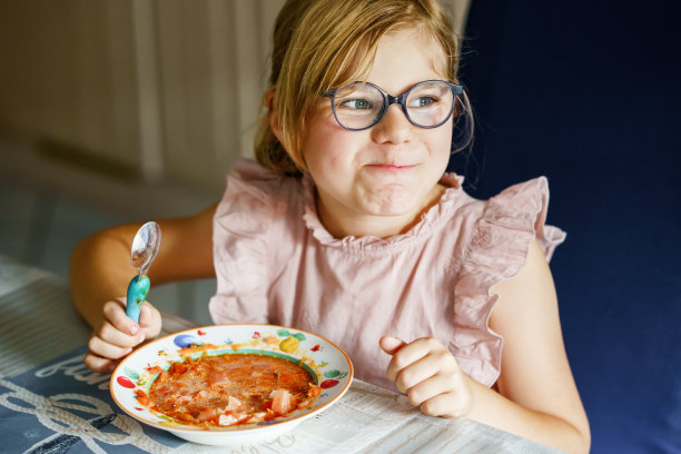 学龄前的小女孩正在用勺子吃蔬菜土豆汤。儿童健康食品。快乐的孩子在家里或托儿所。图片下载