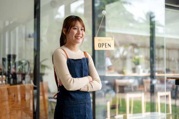 一位漂亮的亚洲女咖啡店老板双臂交叉站在门口。图片下载