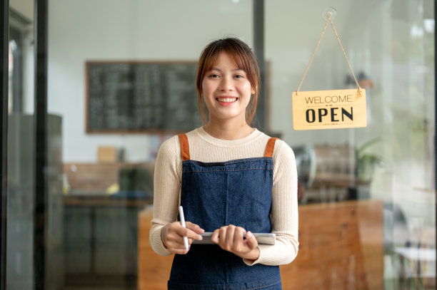 一位漂亮的亚洲女咖啡店老板系着围裙站在门口。图片下载