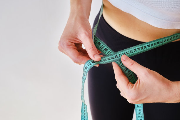 年轻女子细腰上系着一根卷尺。健身教练。营养、训练和正确生活方式的概念。美容与减肥图片下载