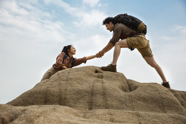 登山者在陡峭的岩石山峰上互相帮助，低角度视图- stock照片图片下载