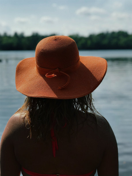 从后面看，湖边的女人戴着橙色的沙滩帽。图片下载