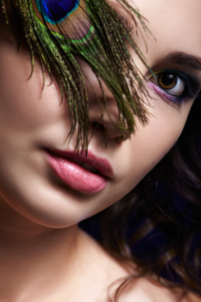 美丽的黑发女人肖像在黑色背景和孔雀羽毛图片下载