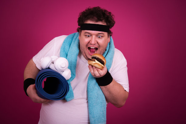 滑稽的胖子正在健身，并且贪婪地吃了一个汉堡包。复古的风格。图片下载