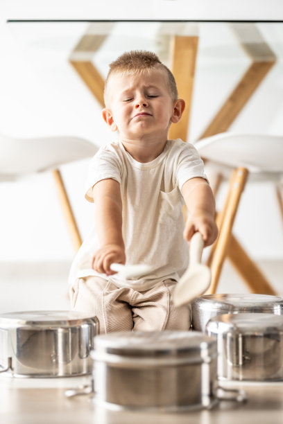 小男孩在锅上打鼓，用木鼓槌当木勺。图片下载