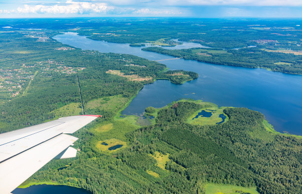 飞机机翼，蓝天，绿色的土地和河流在着陆时的视图。飞机窗口视图。图片下载