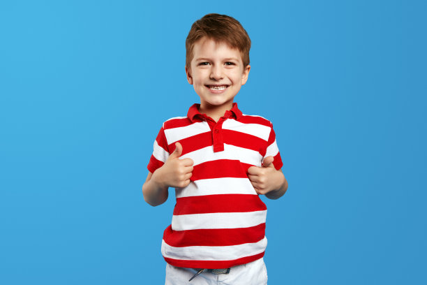 快乐的男孩穿着红色条纹衬衫，摆出喜欢的姿势，带着极度幸福的微笑看着镜头图片下载