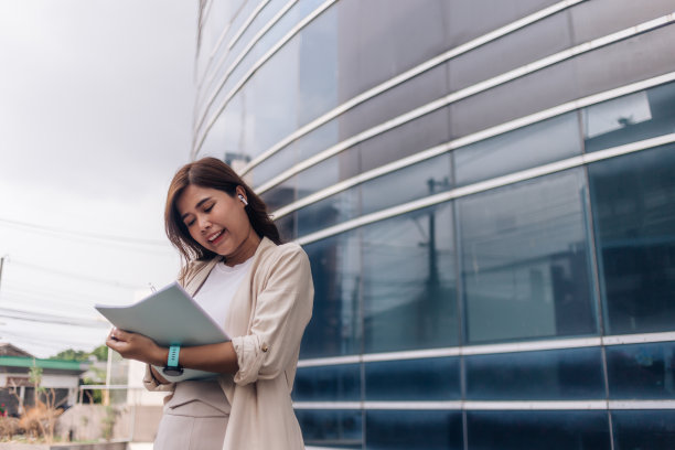 年轻女商人手持笔记本站在办公楼前的肖像图片下载
