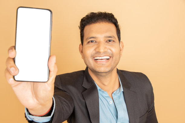 年轻的印度商人穿着西装，展示着空白屏幕的智能手机，将广告隔离在白色背景上。企业的概念。图片下载