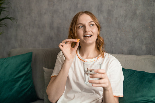 漂亮的年轻女人，坐在家里的沙发上吃着药。高质量照片图片下载