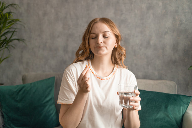 漂亮的年轻女人，坐在家里的沙发上吃着药。高质量照片图片下载