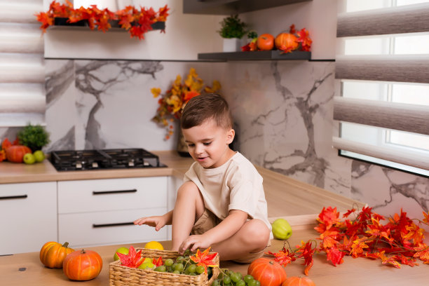 笑容可爱地坐在餐桌上，桌上摆着水果、秋叶和南瓜。秋天装饰的厨房。假期的概念。图片下载
