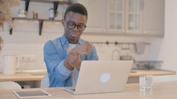 手腕疼痛的非洲年轻人在笔记本电脑上工作图片下载