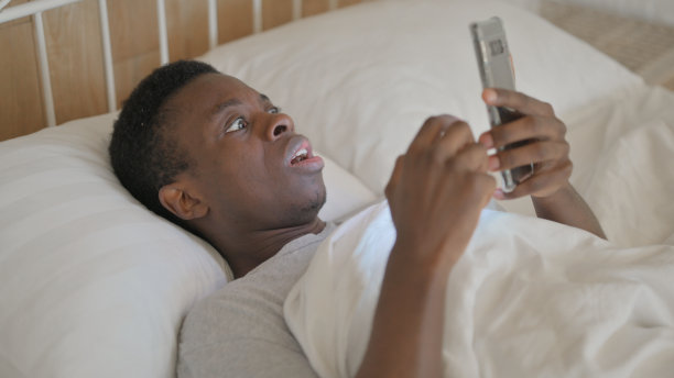 年轻的非洲男子躺在床上被电话丢失震惊图片下载