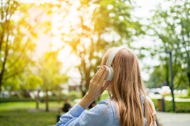 微笑的白人年轻女商人，戴着耳机听着播客电子书、音乐、歌曲、歌手、摇滚乐队，用手机选择音轨，走在城市街道上。高质量照片图片下载