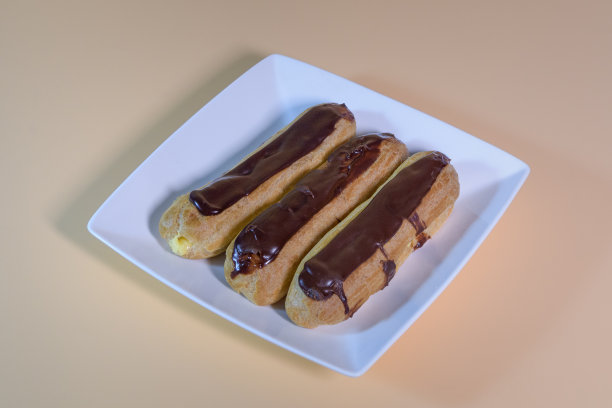 三块新鲜的泡芙放在角落的白色盘子里。在米色背景上图片下载