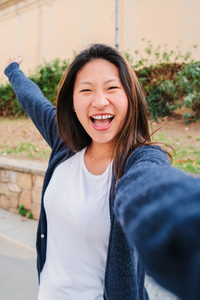 年轻的亚洲黑发女子在自拍时的垂直肖像，微笑着张开双臂。十几岁的快乐女孩开心地看着相机拍了一张个人照片。正面正面正面的女性图片下载