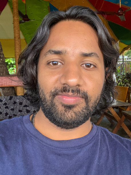 餐厅场景的特写图片，深色胡须的印度男子穿着蓝色t恤的休闲服装，坐在室内，看着相机，肖像，聚焦在前景图片下载