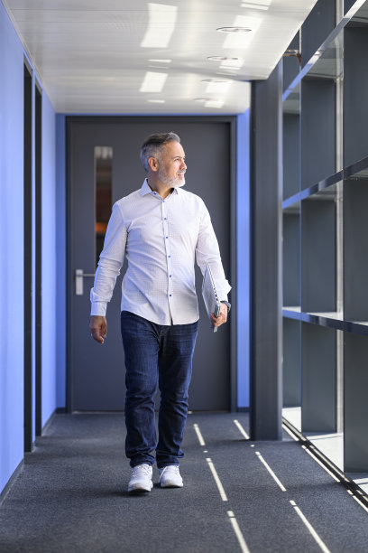 面带微笑的商人拿着笔记本电脑走在走廊里图片下载